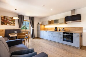 A modern kitchen with grey cabinets, a built-in microwave, and a large oven. There is a dining area with a table and chairs, and a sofa.