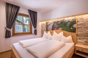 Une chambre avec un grand lit, une fenêtre avec des rideaux, un mur en pierre et un tableau représentant un ours.
