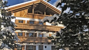 Un chalet à plusieurs étages, doté de balcons en bois et entouré d’arbres couverts de neige.