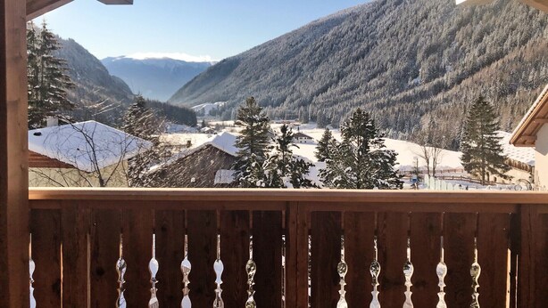 Un balcon en bois offrant une vue sur une vallée et des montagnes enneigées.