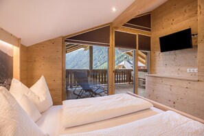 A wooden interior with a bed, a TV mounted on the wall, and a balcony with a view of the mountains. - Apartment 'Lechnerhof Schöne Aussicht' Near the Ski Area with Mountain View, Wi-Fi, Balcony & Garden (Vals)