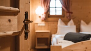 A wooden room with a bed, a nightstand, and a window with curtains. - Cottage 'Lechnerhütte Fane Alm' with Mountain View, Wi-Fi & Terrace (Vals)