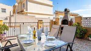 Une table en verre, dressée pour un repas en plein air, offre une vue dégagée sur un bâtiment situé à l’arrière-plan.