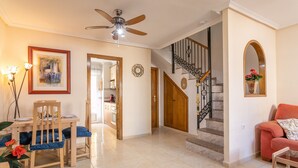 Un grand espace de vie comprenant une table à manger, des chaises, un canapé, un escalier et un ventilateur de plafond.