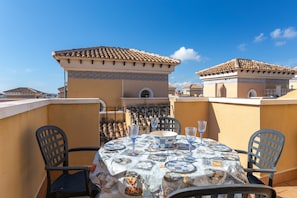 A rooftop terrace with a table set for two, chairs, and a decorative tablecloth.