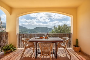Un balcon avec une table, des chaises, un pot de fleurs et une vue sur les montagnes.