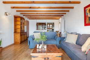 Un salon avec un canapé bleu, une table basse en bois et une cuisine en arrière-plan.
