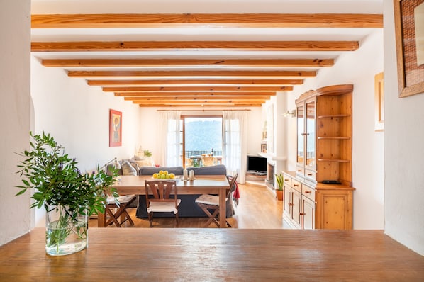 Un coin repas agrémenté de poutres en bois, une table à manger, des chaises, un vase avec des plantes et une vue par la fenêtre.