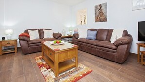 Un salon avec deux canapés en cuir marron, une table basse en bois et un téléviseur posé sur un meuble en bois.