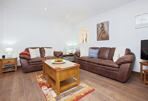 Un salon avec deux canapés en cuir marron, une table basse en bois et un téléviseur posé sur un meuble en bois.
