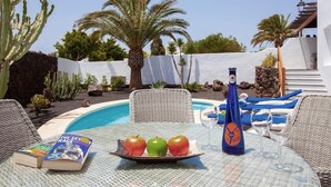 Une table installée au bord de la piscine, avec deux pommes, une bouteille et un livre.