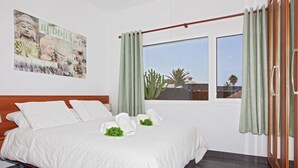 Une chambre d’hôtel avec un lit, une fenêtre avec des rideaux, une œuvre d’art représentant un Bouddha accrochée au mur, et une vue sur un cactus à l’extérieur.