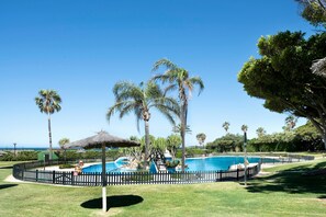 Ein Swimmingpool, umgeben von Palmen und einem Zaun, mit Blick auf den Ozean im Hintergrund.