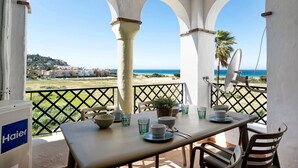 Eine Terrasse mit Esstisch, einem Blumentopf und Blick aufs Meer.