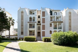 Un immeuble à plusieurs étages doté d’une entrée centrale, de balcons et d’une pelouse bien entretenue.
