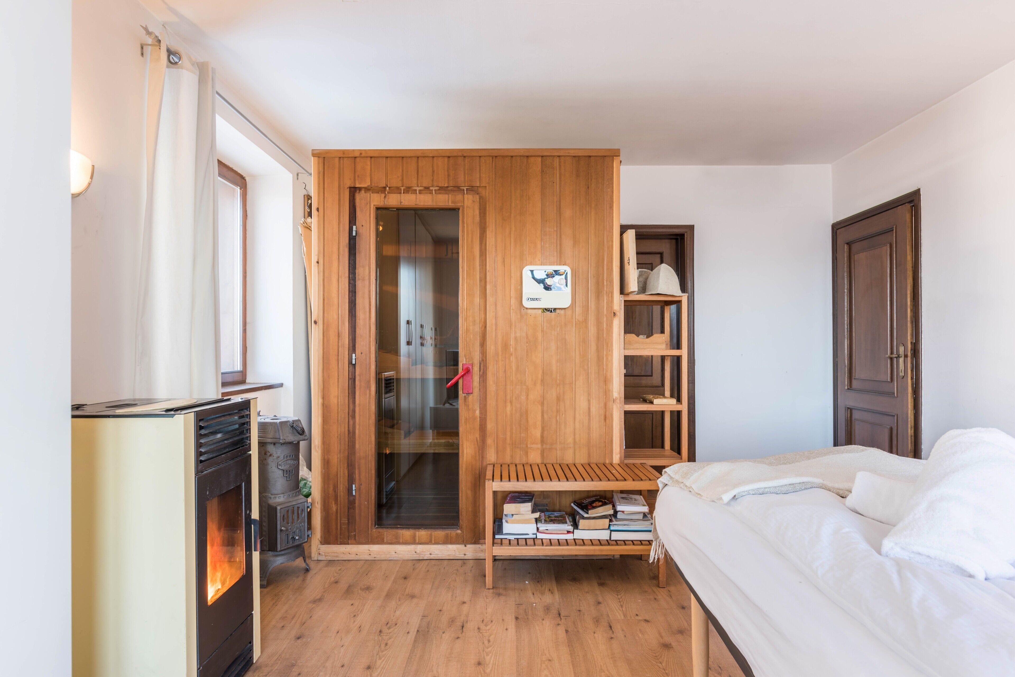 Ein Schlafzimmer mit einem Bett, einem Holzschrank, einem Bücherregal und einem Kaminofen.