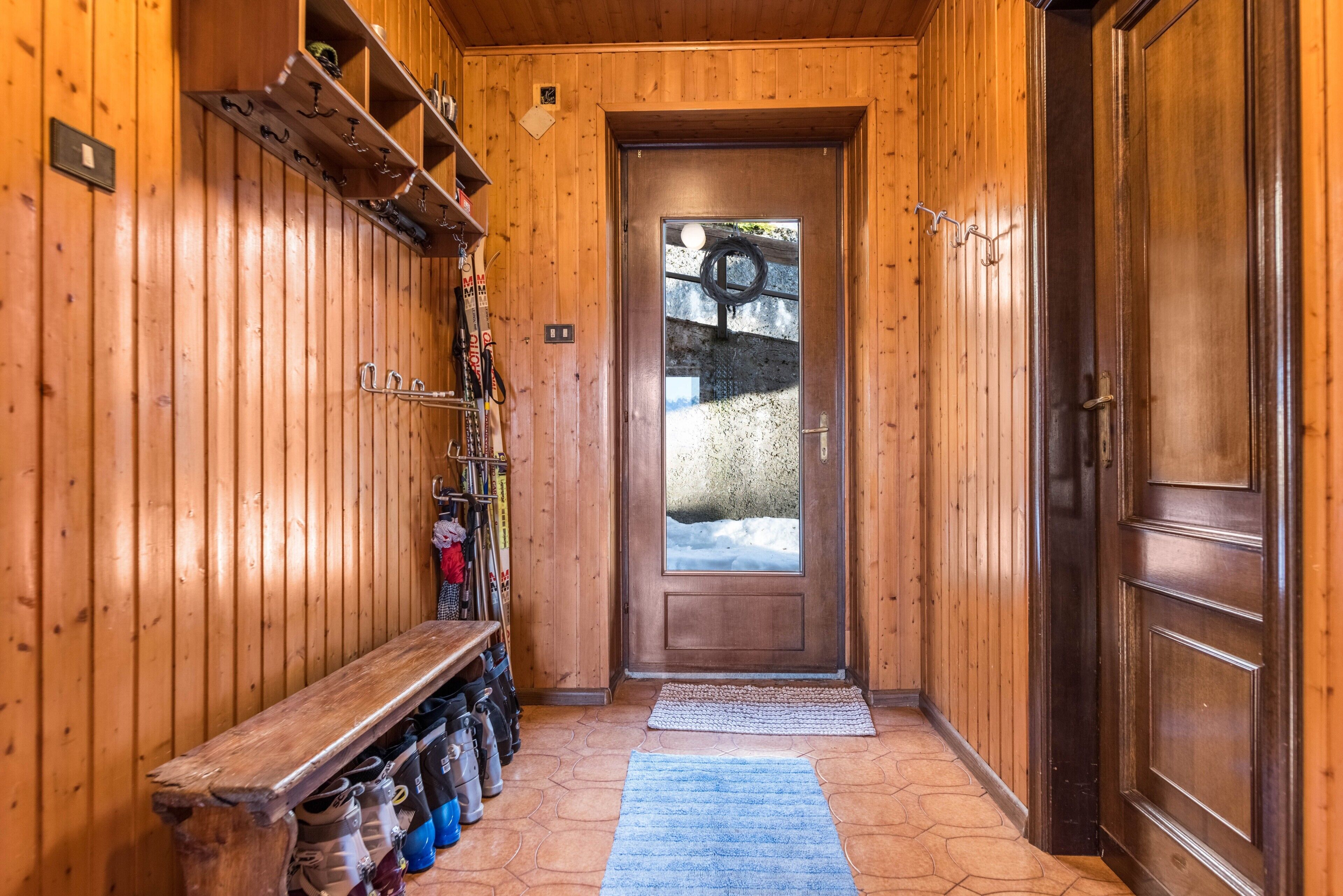 Un corridoio in legno con una panca, un appendiabiti e una porta con un vetro.