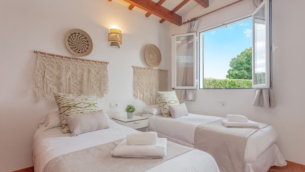Una habitación con dos camas, ventana con vistas, luz empotrada en la pared y un cabecero de macramé.