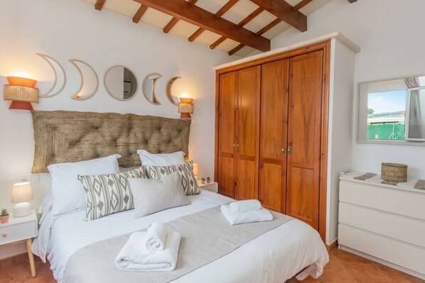 A bedroom with a bed, wooden wardrobe, wall sconces, and a window.