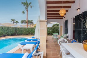 Un espace aménagé au bord de la piscine, avec des chaises longues, une table et un luminaire suspendu.