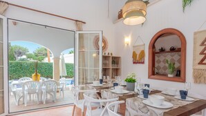 Een eethoek met witte stoelen en een houten tafel, een glazen deur naar buiten en een wand met een spiegel en decoratieve objecten.