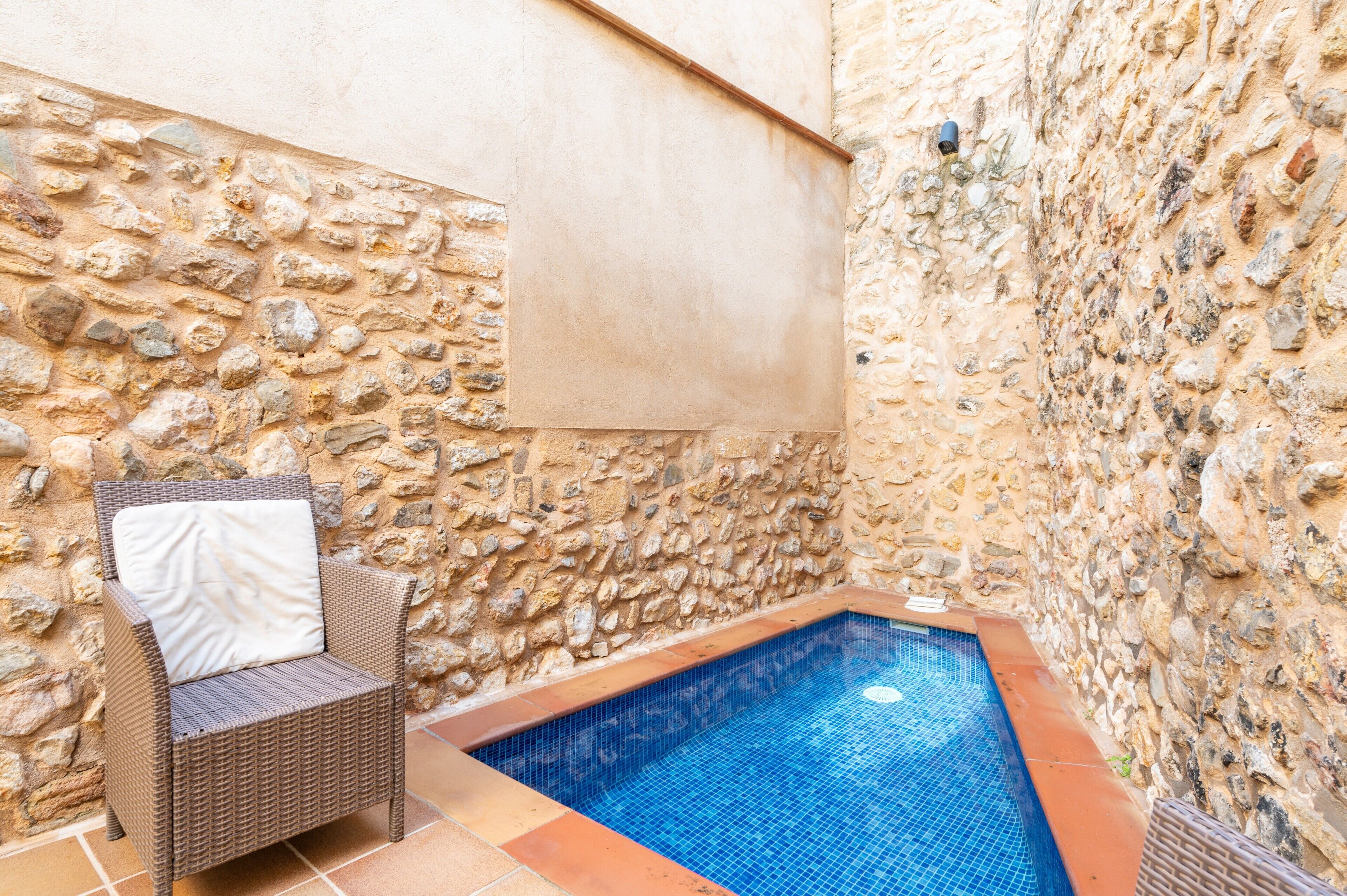 Un espace piscine entouré de murs en pierre, avec un fauteuil en osier et une serviette.