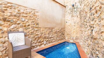 Un espace piscine entouré de murs en pierre, avec un fauteuil en osier et une serviette.