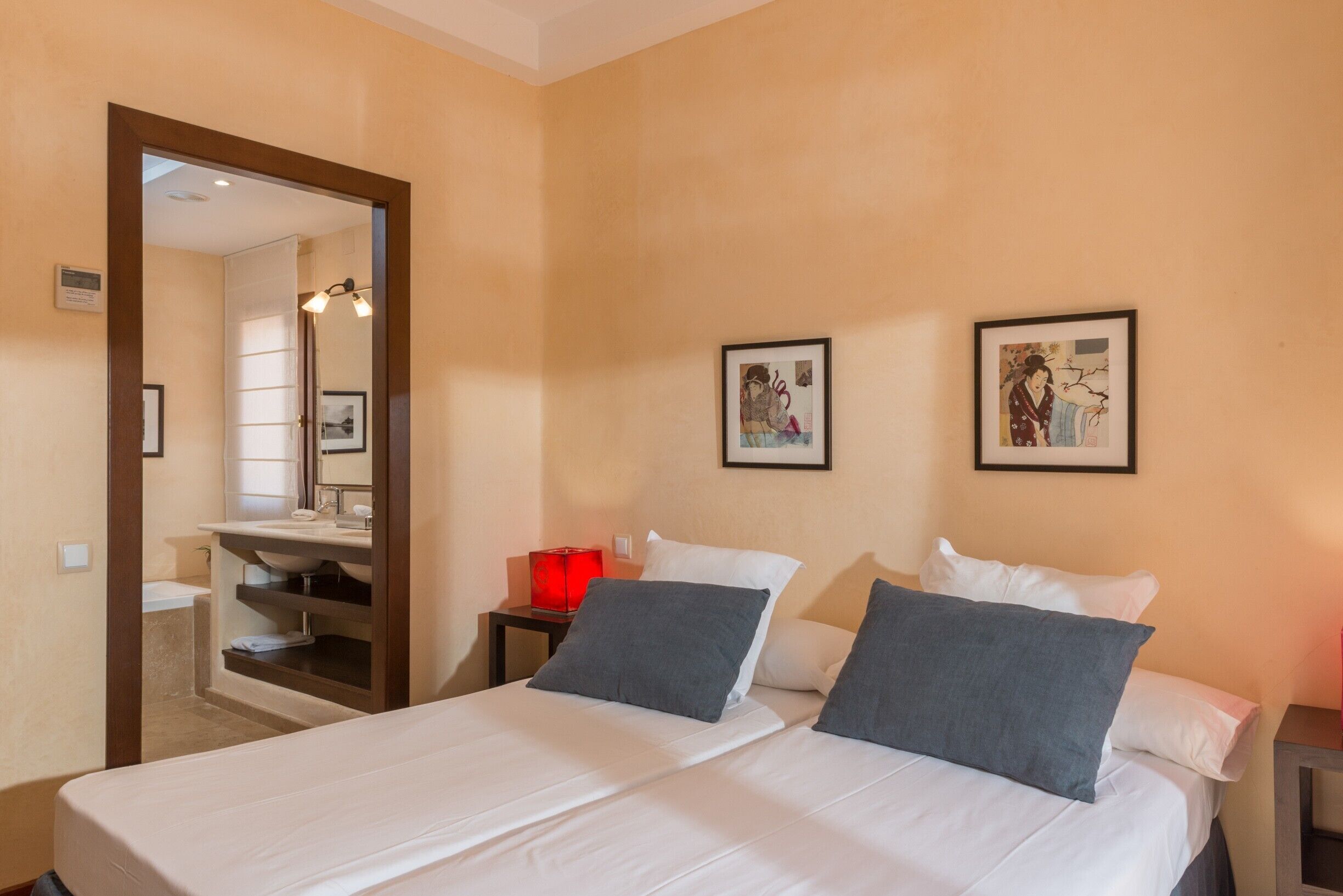 Una habitación de hotel con cama, mesita de noche, espejo y dos cuadros en la pared.
