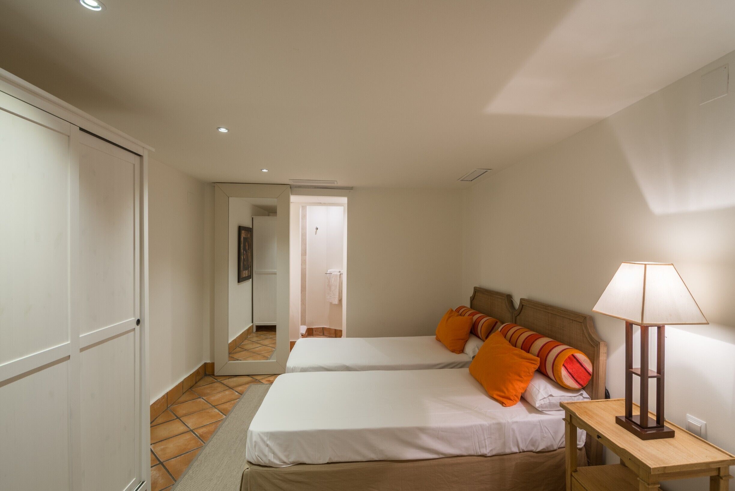 Una habitación de hotel con dos camas, una mesita de noche, una lámpara y un espejo.