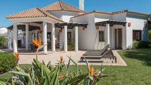 A two-story house with a tiled roof, a covered patio, and a garden with tropical plants. - Villa Lila with Private Pool, Garden and Wi-Fi (Benalup Casas Viejas)