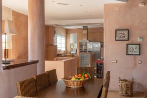 Una cocina moderna con una isla central, un comedor con mobiliario de mimbre y un cuadro colgado en la pared.