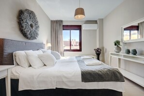 A modern hotel room with a large bed, a bedside table, a mirror, and a view of the cityscape.