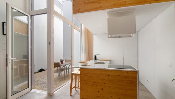 Een moderne keuken met een houten eiland, een eethoek met tafel en stoelen, en een schuifdeur van glas die leidt naar een buitenruimte.