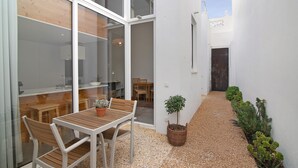 Een terras met een tafel, stoelen, een bloempot en een grindpad dat naar een deur leidt.