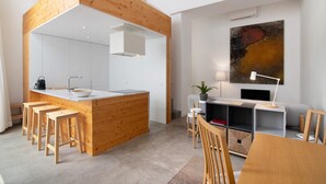 Een moderne keuken met houten details, een eethoek met een houten tafel en stoelen, en een groot abstract schilderij aan de muur.