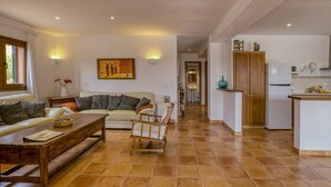 A living room with a sofa, coffee table, and a wooden bench. There is a kitchen area with a refrigerator and a sink. - House with Private Pool, Mountain Views, and Wi-Fi in Begur (Begur)