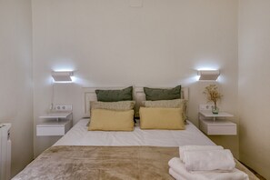 A neatly arranged bedroom with a bed, two bedside tables, a nightstand, and a wall-mounted lamp.