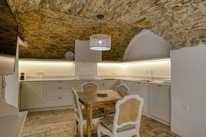 A rustic stone ceiling, a wooden dining table with chairs, and a modern pendant light.