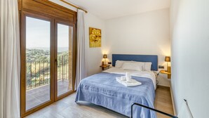 A hotel room with a bed, two bedside lamps, a painting, a balcony with curtains, and a view of the landscape. - Apartment 'Residencial  2º 2ª' with Shared Terrace, Balcony and Wi-Fi (Begur)