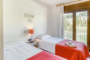Habitación de hotel con dos camas, una mesita de noche, una lámpara y un balcón con vistas.