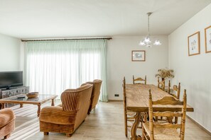 Un coin repas avec une table et des chaises en bois, un téléviseur et une fenêtre ornée de rideaux légers.