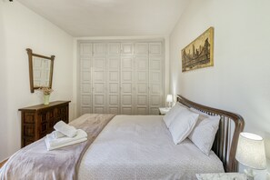 A bedroom with a bed, a dresser, a mirror, a door, and a wall-mounted lamp.