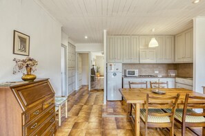 Een keuken met houten kastjes, een eettafel, stoelen, een koelkast en een magnetron.