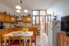 Een keuken met houten kastjes, een eettafel met stoelen, een koelkast en een televisie.