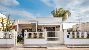 A white building with a gated entrance, a small porch, and a palm tree in the background.