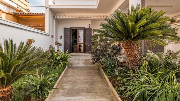 A pathway leading to a building with a door, surrounded by lush greenery and a clear sky.