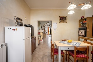 Een keuken met een koelkast, een eettafel met stoelen en een gang naar een andere kamer.