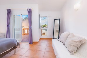 A bedroom with a bed, a sofa, a mirror, and a balcony with curtains.