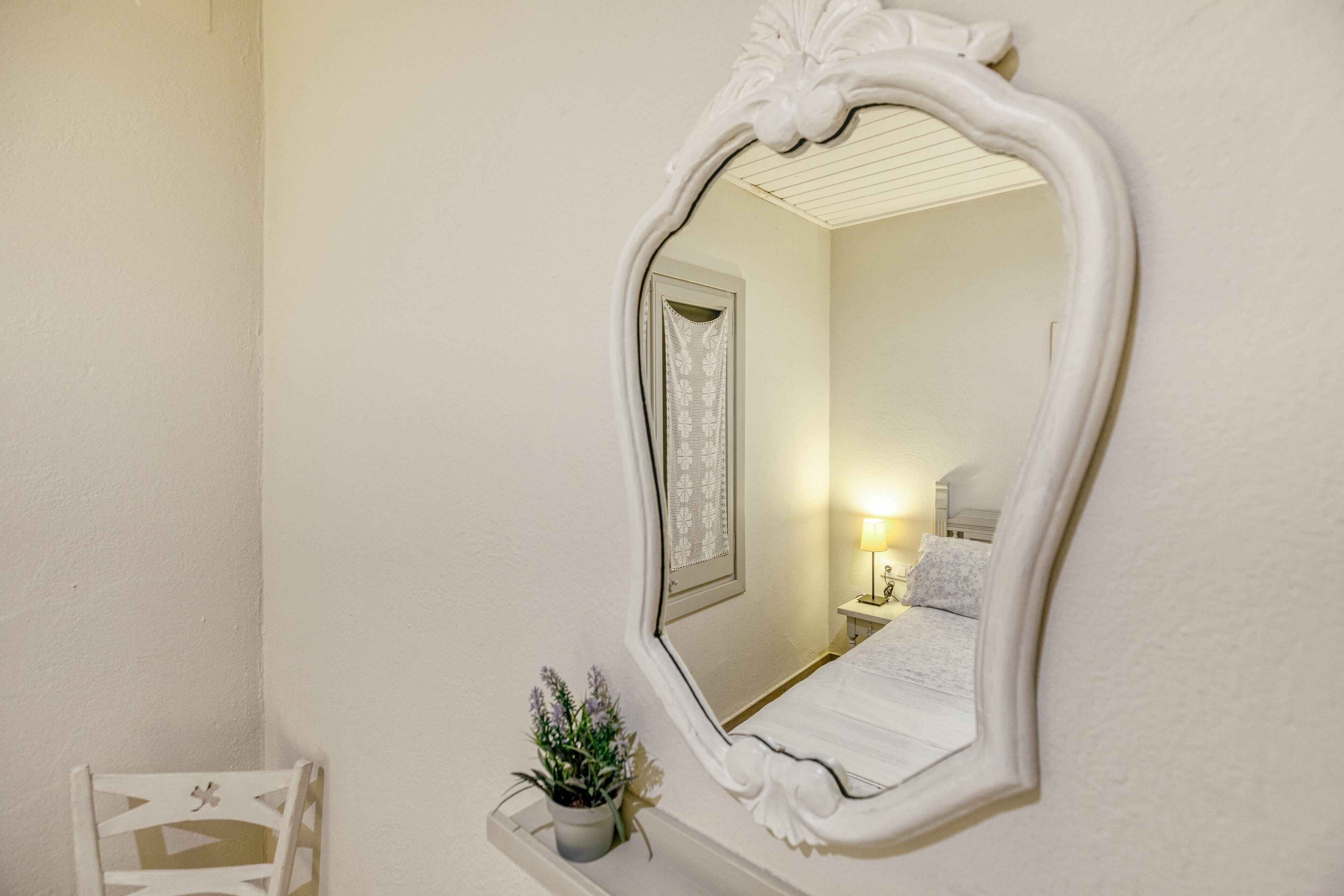 Un miroir avec un cadre orné, une table de chevet avec une lampe et une petite plante en pot accrochée au mur.