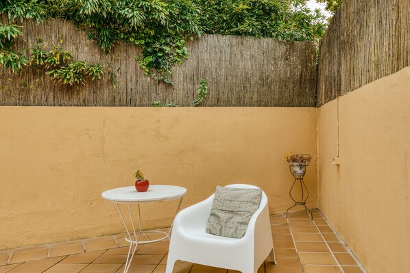 A small patio area with a white chair, a small round table, and a potted plant.